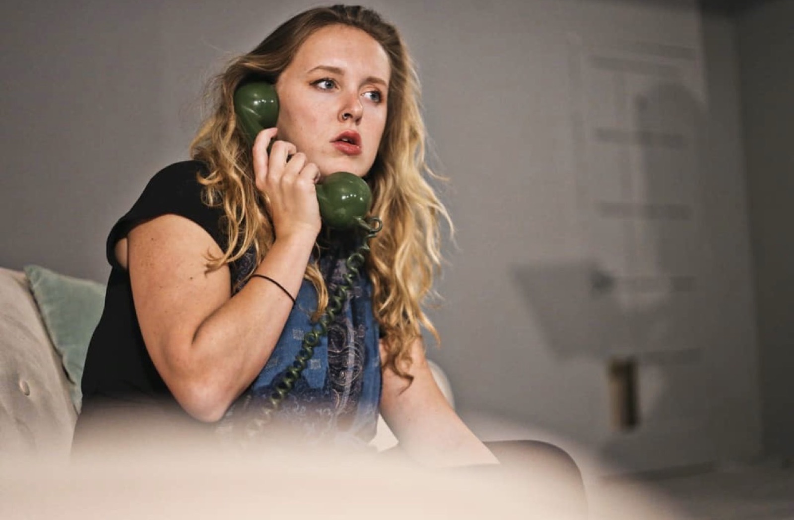 Close-up of a performer holding a green rotary telephone receiver to her ear