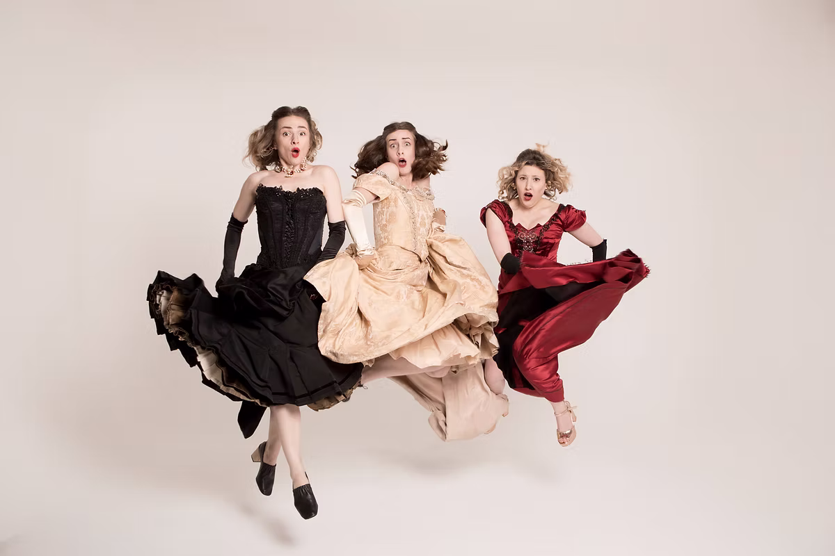 Three performers in black, gold, and red ballgowns leap mid-air with shocked expressions for Anna Kareni Na Na Na