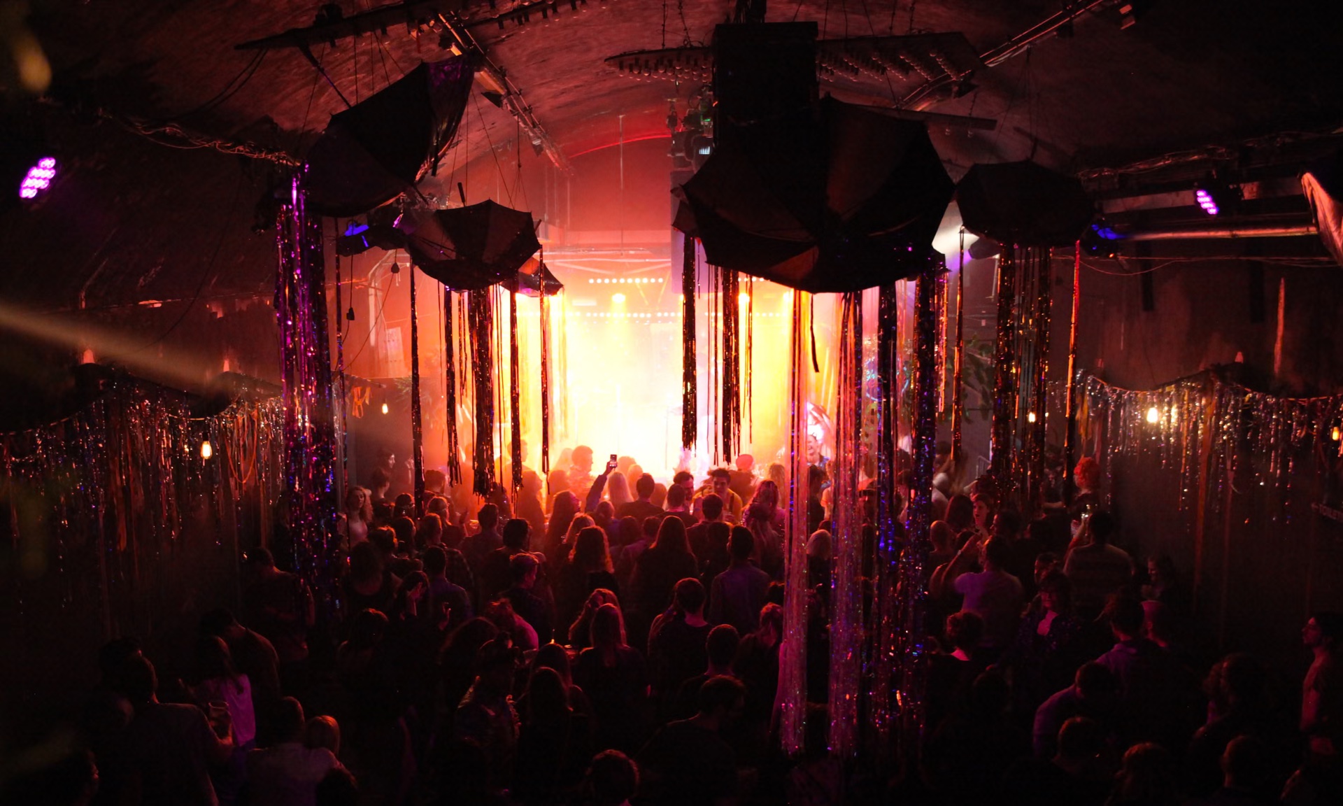 A crowd dances beneath tinsel streamers and warm stage lighting at a late night party in the venue