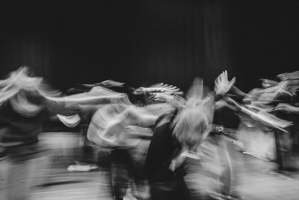 A long-exposure photo of performers mid-movement on stage, their bodies blurred into streaks of motion